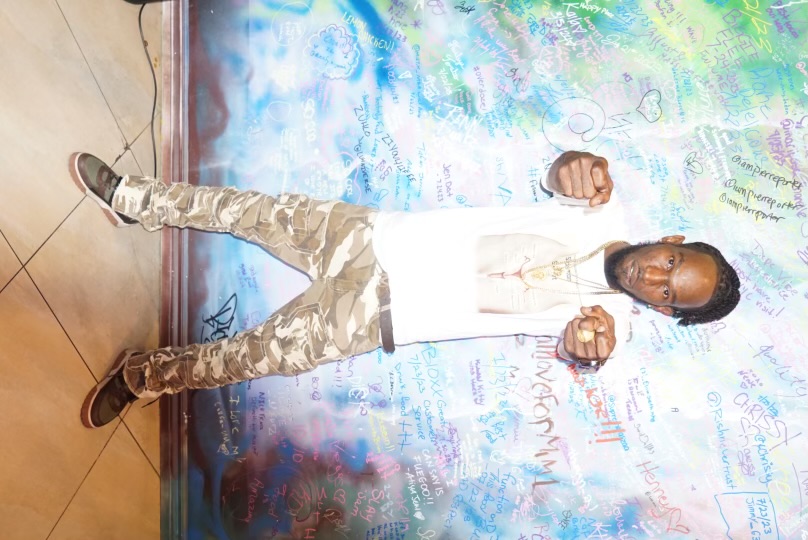 Original AcMoney portrait in a white shirt and camouflage trousers